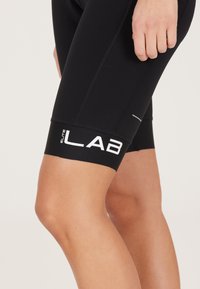 Mustat pyöräilyshortsit, jotka on valmistettu joustavasta materiaalista. Niissä on paksu musta vyötärönauha, jossa on valkoinen "Elite LAB" -logo ja sileä pinta.