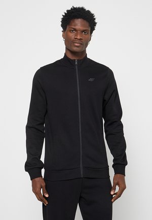 Chaqueta negra de cremallera con un cuello alto, hecha de una tela suave, con bolsillos laterales y un logo sutil en el pecho.