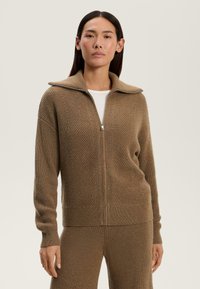 Pulover cu fermoar de culoare marron, cu un guler înalt, având un model texturat tip herringbone și manșete cu riburi. Fabricat dintr-un material tricotat moale și călduros.