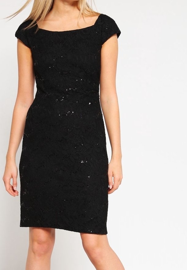Robe noire mi-genou avec manches courtes et détails subtils en sequins portée par une femme debout sur un fond uni.