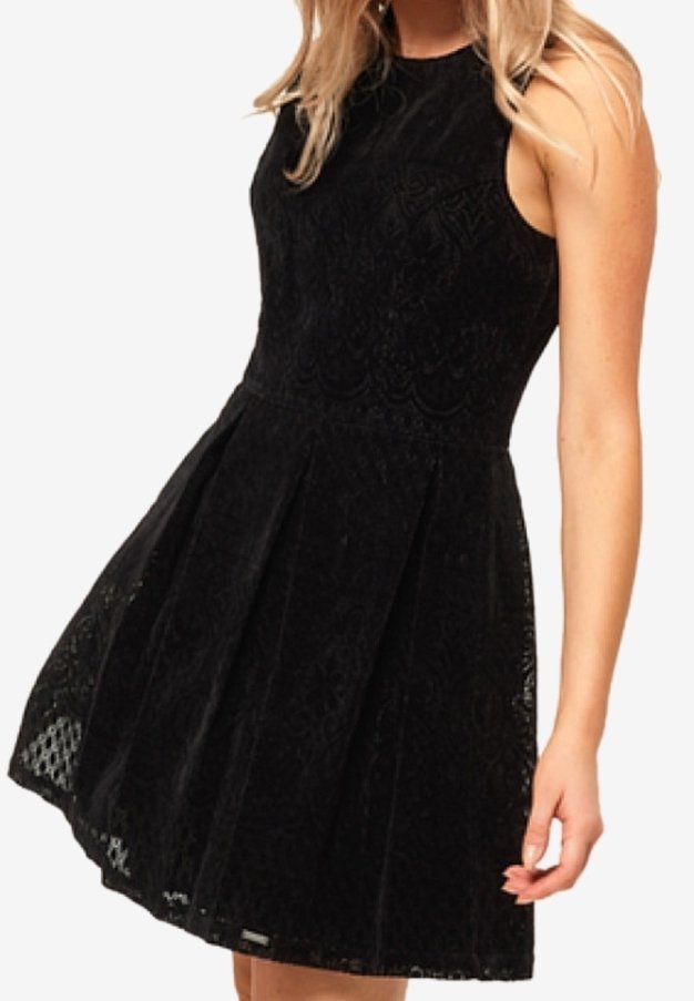 Femme portant une robe noire en dentelle sans manches avec un corsage ajusté et une jupe évasée, se tenant devant un fond uni.