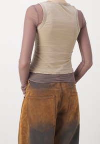 Beige linne över en brun genomskinlig långärmad skjorta, parat med bruna texturerade kordbyxor med blekningar och fickdetaljer.