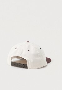 Casquette snapback réglable avec un tissu couleur crème, une visière marron et des œillets de ventilation marron, vue de l'arrière sur un fond clair.
