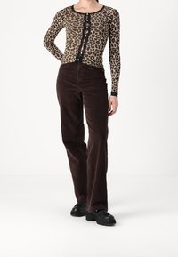 Top a maniche lunghe con stampa leopardata, rifinito con pizzo e bottoni, abbinato a pantaloni a gamba larga in velluto a coste marrone e sneakers chunky nere.