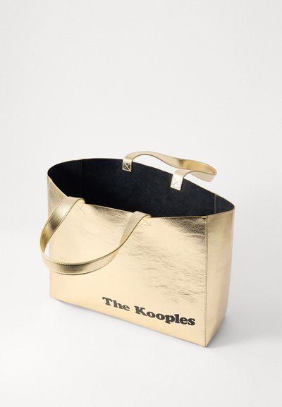 Zlatna metalik torba s crnim unutrašnjim dijelom, s dva ručka i otisnutim logotipom "The Kooples" u crnoj boji na prednjoj strani. Glatka tekstura.