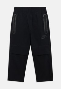 Črne Nike hlače z elastičnim pasom, dvema žepoma na zadrgo in logotipom. Tkanina ima gladko teksturo in oprijet kroj.