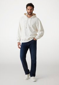 Hvid hoodie med tonale præget mønstre, snøre og ribbede manchetter, parret med mørkeblå jeans og hvide sneakers.