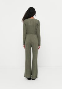 Set din două piese de culoare verde măslin, cu o bluză cu mânecă lungă și pantaloni evazați, evidențiind o textură netedă și o siluetă ajustată.