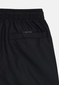 Svarte shorts med elastisk liv, med en baklomme som inkluderer en Calvin Klein etikett. Glatt tekstur, enkelt design.