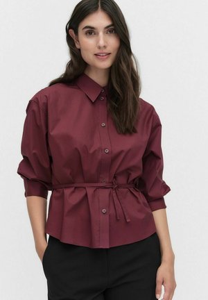 Maroon button-up shirt with a collar, gathered cuffs, and a tie waist detail, crafted from a smooth, lightweight fabric.