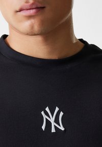 Black cotton t-shirt with a round neckline and white embroidered "NY" logo on the left side. Smooth texture, fitted design.