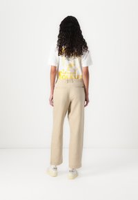 T-shirt bianca con grafica gialla che presenta il testo "Lemon Squeezy" abbinata a pantaloni beige a gamba larga e sneaker bianche.