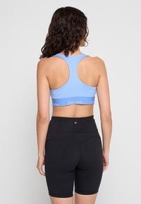 Blaues sportliches Crop-Top mit Racerback-Design und Logoband, kombiniert mit hoch taillierten schwarzen Shorts; glatte Textur, figurbetonter Stil.