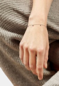 Pulsera de plata con cinco pequeñas piedras preciosas azules a lo largo de una delicada cadena, llevada en una mano que descansa sobre una tela de punto texturizada.