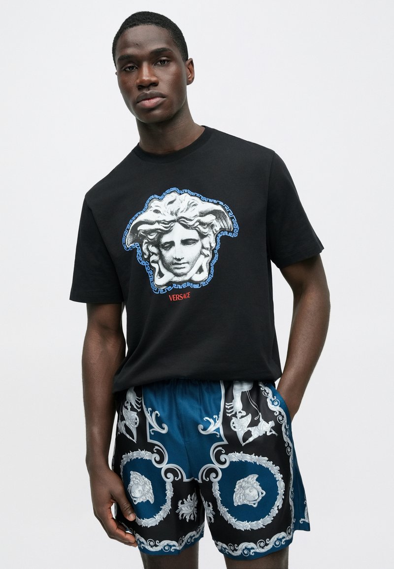 Sort bomuld T-shirt med et centralt motiv af et klassisk ansigt; kombineret med mønstrede shorts i blå, sort og hvid med indviklede designs.