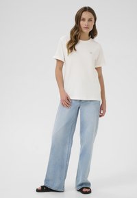 White cotton t-shirt with rolled sleeves, featuring a small embroidered detail, paired with light blue wide-leg jeans and black sandals.