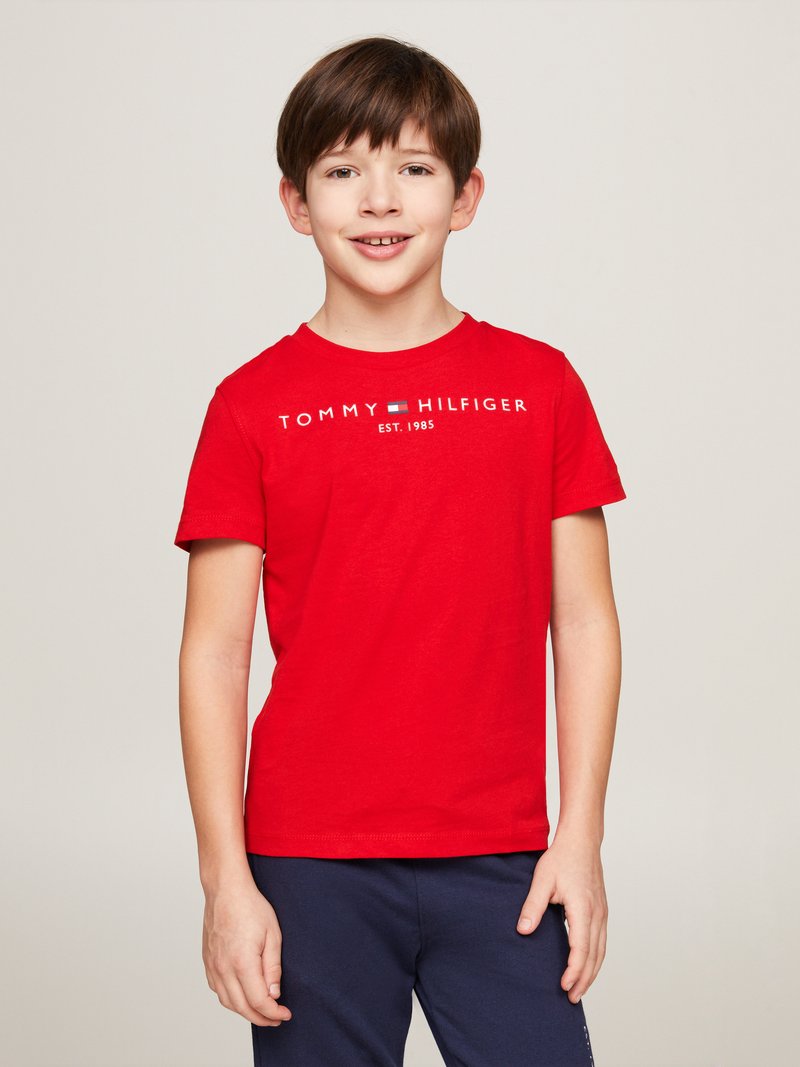 Sarkanas kokvilnas T-krekls ar īsām piedurknēm, apaļo kakla izgriezumu, ar baltu tekstu „TOMMY HILFIGER EST. 1985” uz krūšu daļas.