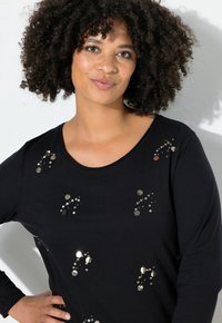 Zwarte top met lange mouwen, voorzien van cirkelvormige zilveren pailletten in patronen gerangschikt. Zachte stof met een ronde hals en een losse pasvorm.