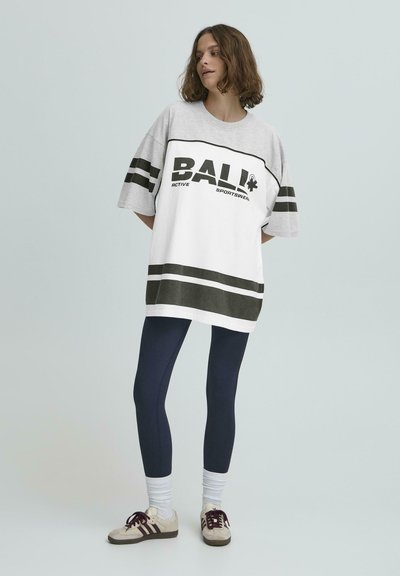 Prelarge šedé a biele tričko s čiernym písmom a pruhovanými akcentmi, spárované s námorníckymi legínami a béžovými teniskami.