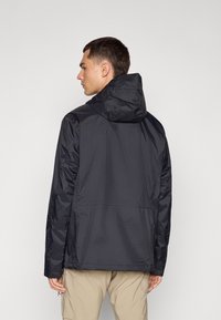 Veste légère noire avec capuche, affichant une texture lisse et un design simple. La vue arrière montre des coutures minimales et une coupe décontractée.