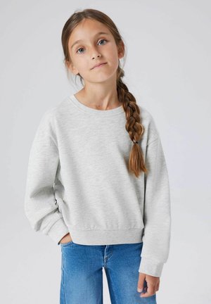 Jasnoszara bluza z okrągłym dekoltem i ściągaczami, zestawiona z niebieskimi dżinsami. Miękka faktura, casualowy krój, bez widocznych wzorów.