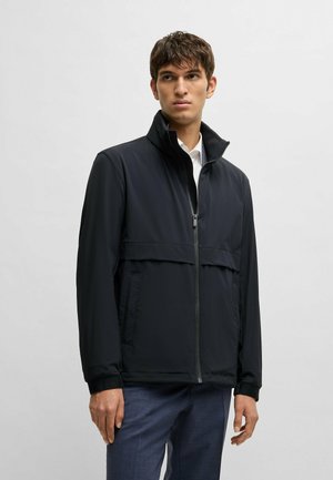Giacca nera con zip, colletto alto, pannello superiore testurizzato e tasche laterali. Presenta polsini elasticizzati e un tessuto liscio.