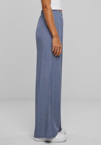 Pantalon large à rayures bleues avec une taille élastique, présentant une texture de tissu lisse et une coupe ample, associé à des baskets blanches.