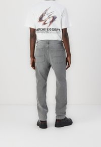 Pantalones vaqueros de algodón grises con un corte relajado, que cuentan con dos bolsillos traseros. Se combinan con una camiseta blanca con un diseño gráfico que muestra texto y logo coloridos.