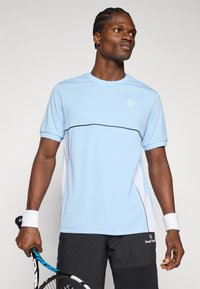 Camiseta atlética de color azul claro con ribetes negros, cuello redondo y mangas cortas. Llevada con pantalones cortos oscuros; sostiene una raqueta de tenis.