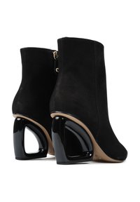 Para czarnych zamszowych botków za kostkę z unikalnymi, wyciętymi, błyszczącymi czarnymi blokami obcasów i beżowymi podeszwami, pokazanymi z tyłu i z boku.