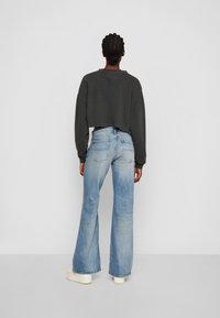 Grå kortad sweatshirt parat med ljusblå utsvängda jeans. Jeansen har en blekt effekt och bakfickor. Vita plattformssneakers synliga.