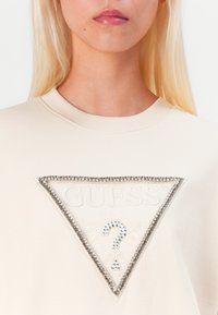 Felpa beige con logo a triangolo e testo in rilievo, arricchita con strass. Collo a costine e texture del tessuto morbida.
