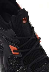 Chaussure de sport noire avec une tige en tricot texturé, des accents orange et des lacets noirs. Comprend une languette et une semelle en caoutchouc pour une traction optimale.