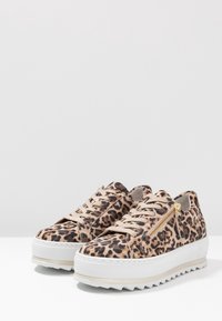 Baskets imprimées léopard avec des motifs beiges et noirs, matériau texturé, détail de fermeture éclair doré et semelle extérieure épaisse blanche avec bonne traction.