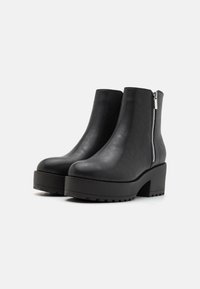 Botines negros con un acabado de piel lisa, tacón cuadrado, suela con plataforma y cremallera lateral para un fácil uso. Suela con textura para mayor agarre.