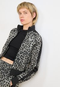 Giacca in stampa leopardata realizzata in tessuto leggero, con colletto alto, dettagli neri, chiusura con zip e logo Puma sul petto.