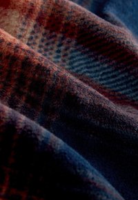 Wool fabric with a textured surface featuring a plaid pattern in deep blue, burgundy, and orange tones, highlighting rich color variations.