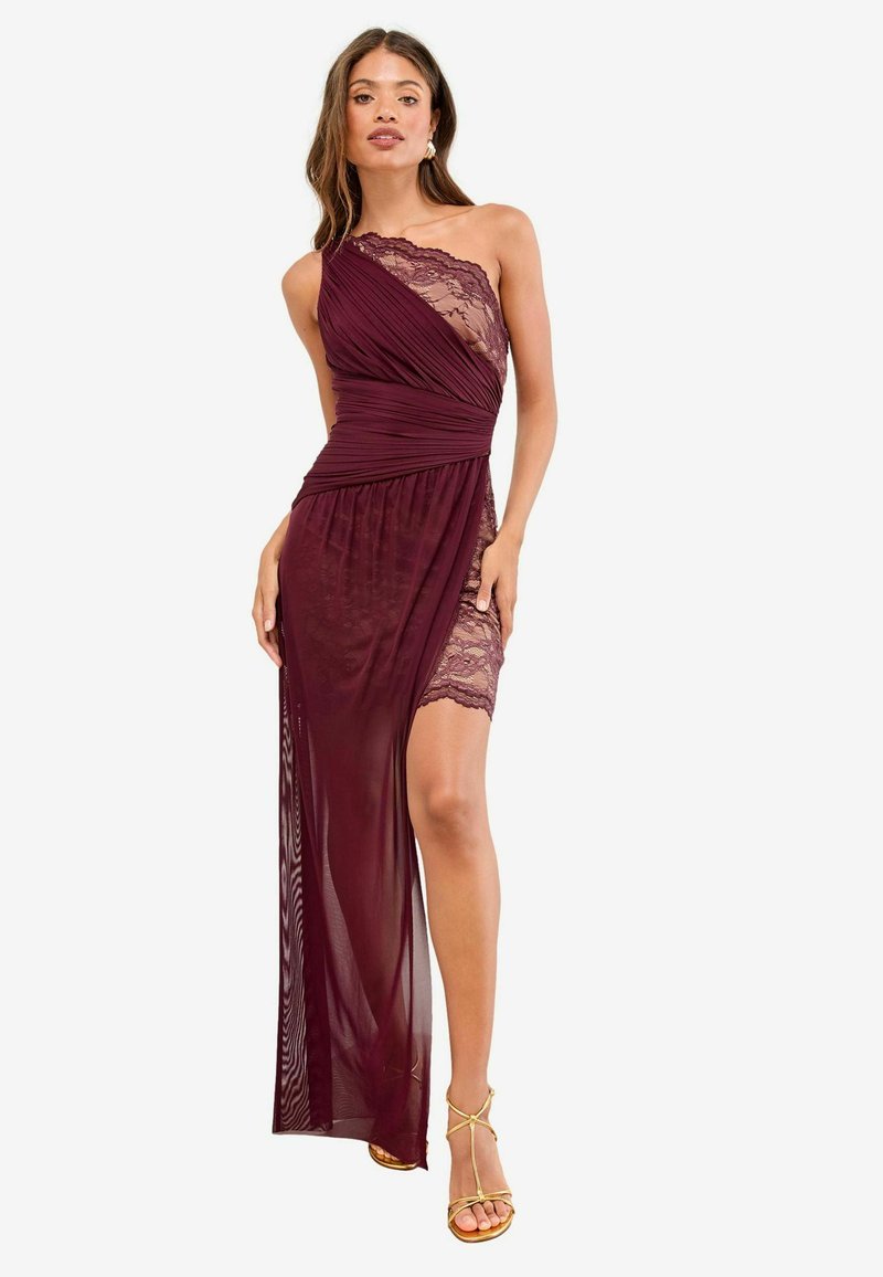 Frau trägt ein burgunderfarbenes Kleid mit einem Schulterträger, das mit Spitze verziert ist und einen transparenten Überzug hat, kombiniert mit goldenen, hohen Sandalen mit Riemchen.