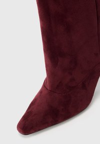 Stivale ankle in suede bordeaux con punta affusolata, superficie leggermente testurizzata e alto tacco a stiletto. Presenta un design senza cuciture.