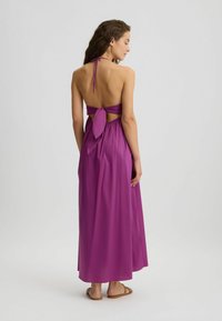 Maxi dress in vibrant purple, made of lightweight fabric. Features a halter neck, open back, and tied waist detail. Flowy design with minimal texture.