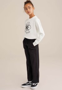 White sweatshirt with black floral outline design and text; paired with loose black trousers and black sneakers with white soles.