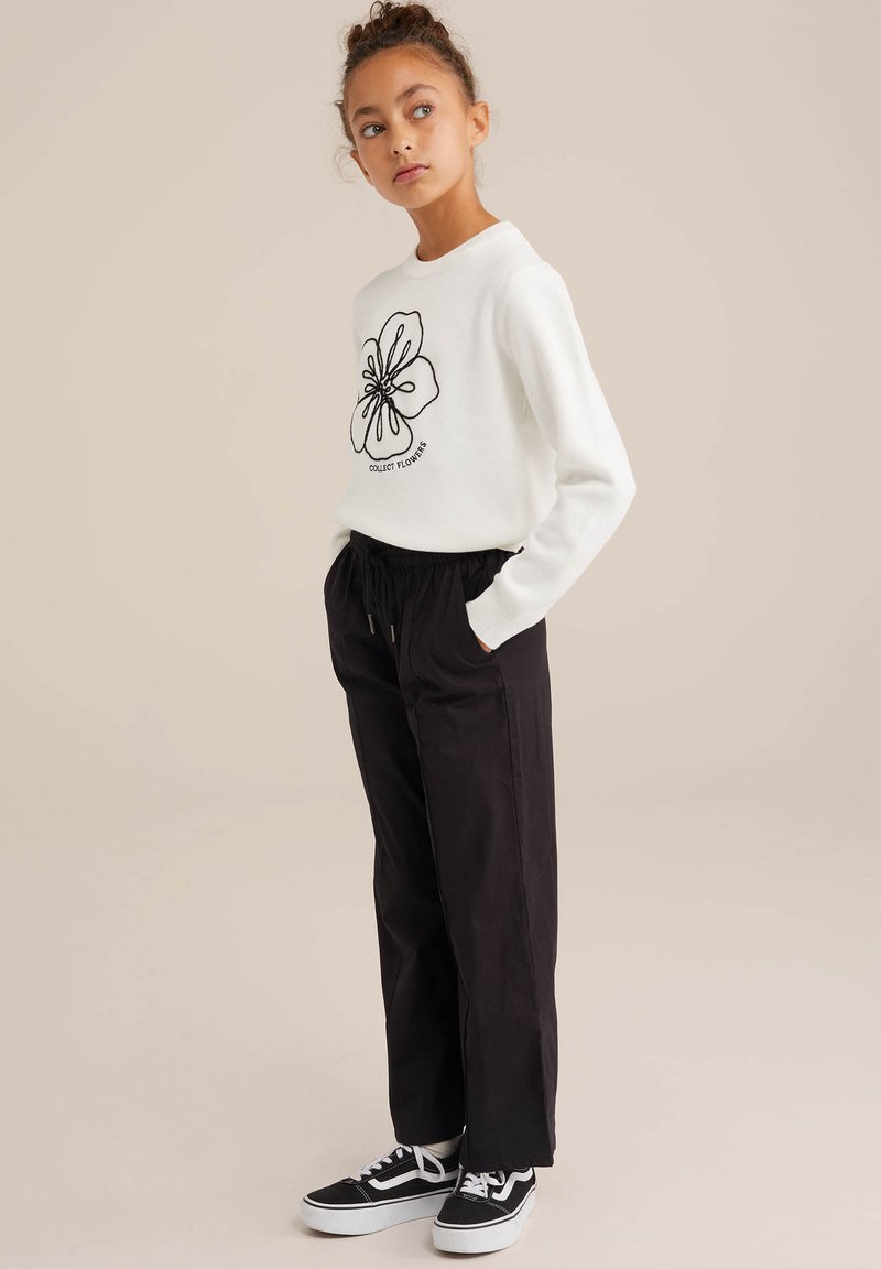 White sweatshirt with black floral outline design and text; paired with loose black trousers and black sneakers with white soles.