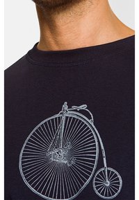 Sweatshirt bleu marine arborant un graphique de bicyclette penny-farthing vintage en gris clair. Le col côtelé et la texture offrent un ajustement confortable.