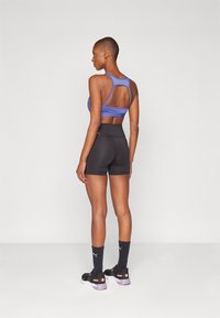 Sportsbeklædning bestående af en lilla sports-bh med racerback-design, sorte højtaljede shorts og sorte sneakers med pink detaljer.