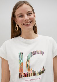 Camiseta de algodón blanca con un vibrante diseño gráfico en varios colores de "LC". Cuello redondo y mangas cortas; corte simple y relajado.