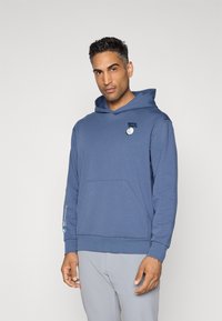 Hoodie azul feito de tecido macio, com um bolso frontal e um patch de logotipo. Projetado com um ajuste relaxado e capuz ajustável com cordão.