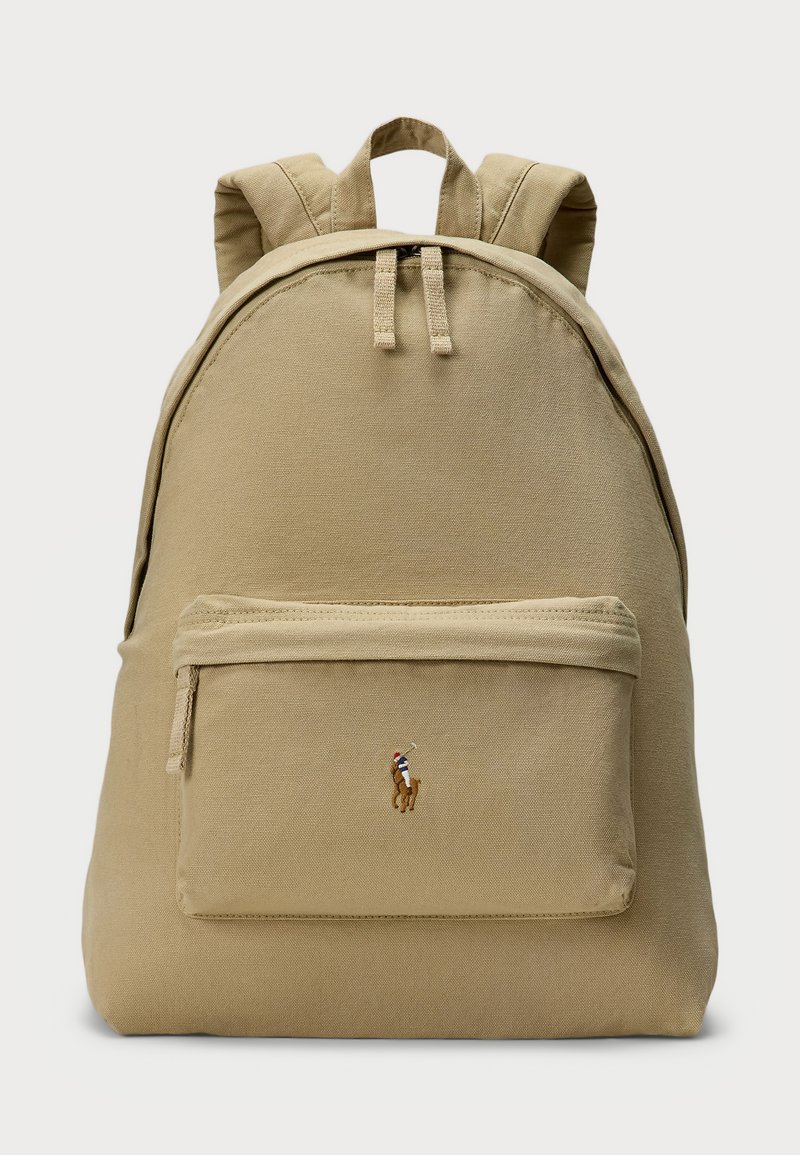 Μπεζ σακίδιο φτιαγμένο από ύφασμα με στρογγυλό σχήμα, μπροστινός θησαυρός με φερμουάρ και κεντημένο λογότυπο. Δύο ιμάντες για μεταφορά, υφασμάτινη επιφάνεια.