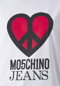 Bílé tričko s velkým červeným srdcem a symbolem míru, a tučným textem pod ním "MO5CH1NO JEANS."