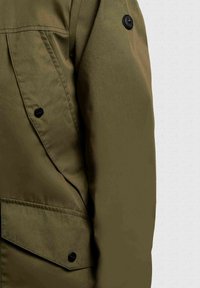 Olijfgroene jas met zichtbare zwarte knopen en een schuin geplaatste klepzak op een effen lichte achtergrond.