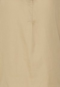 Chemise en lin beige clair avec une coupe décontractée, un demi-fermoir et une texture subtile, idéale pour un look décontracté.